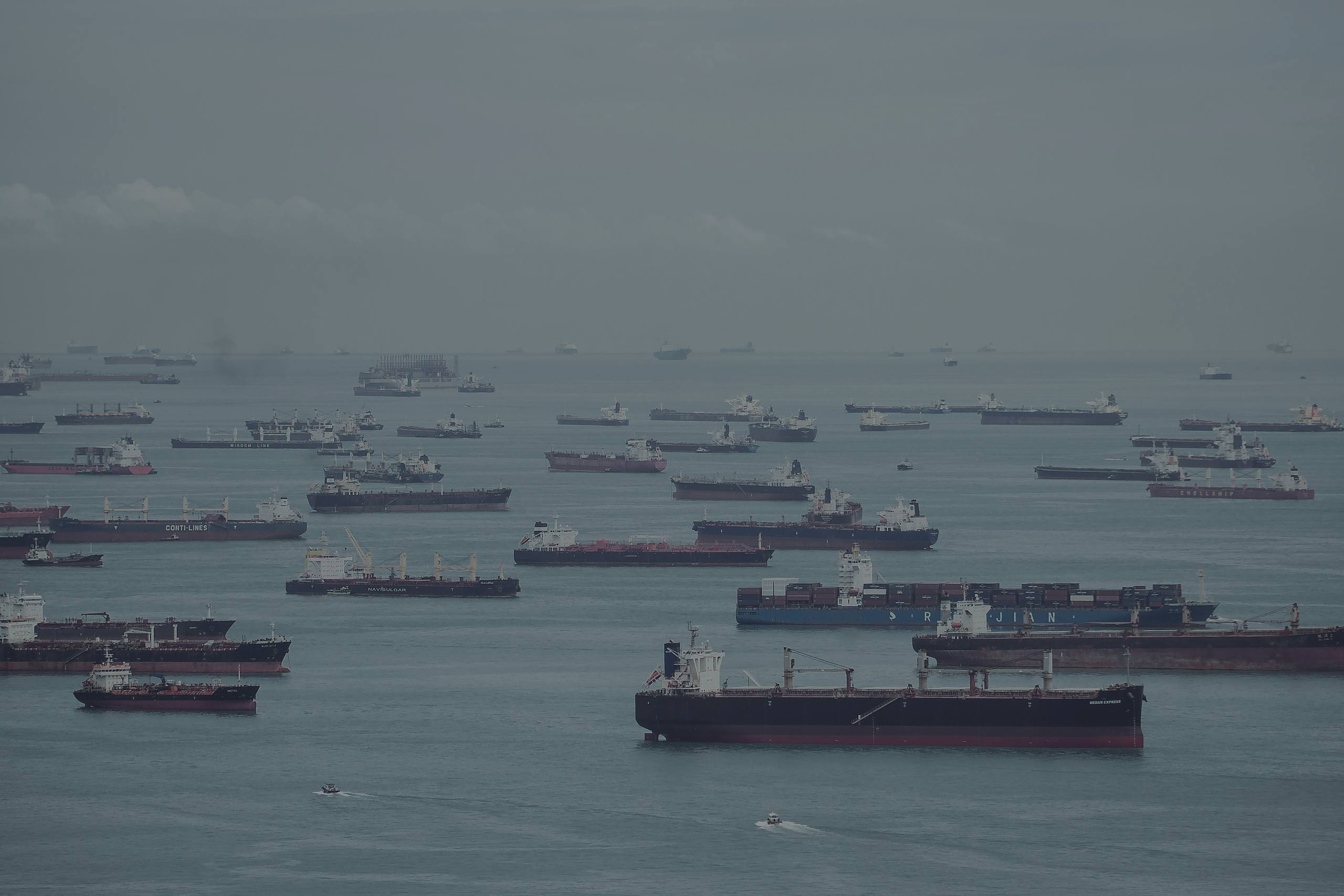 A hazy tropical anchorage, ships of every kind riding at anchor across the water.