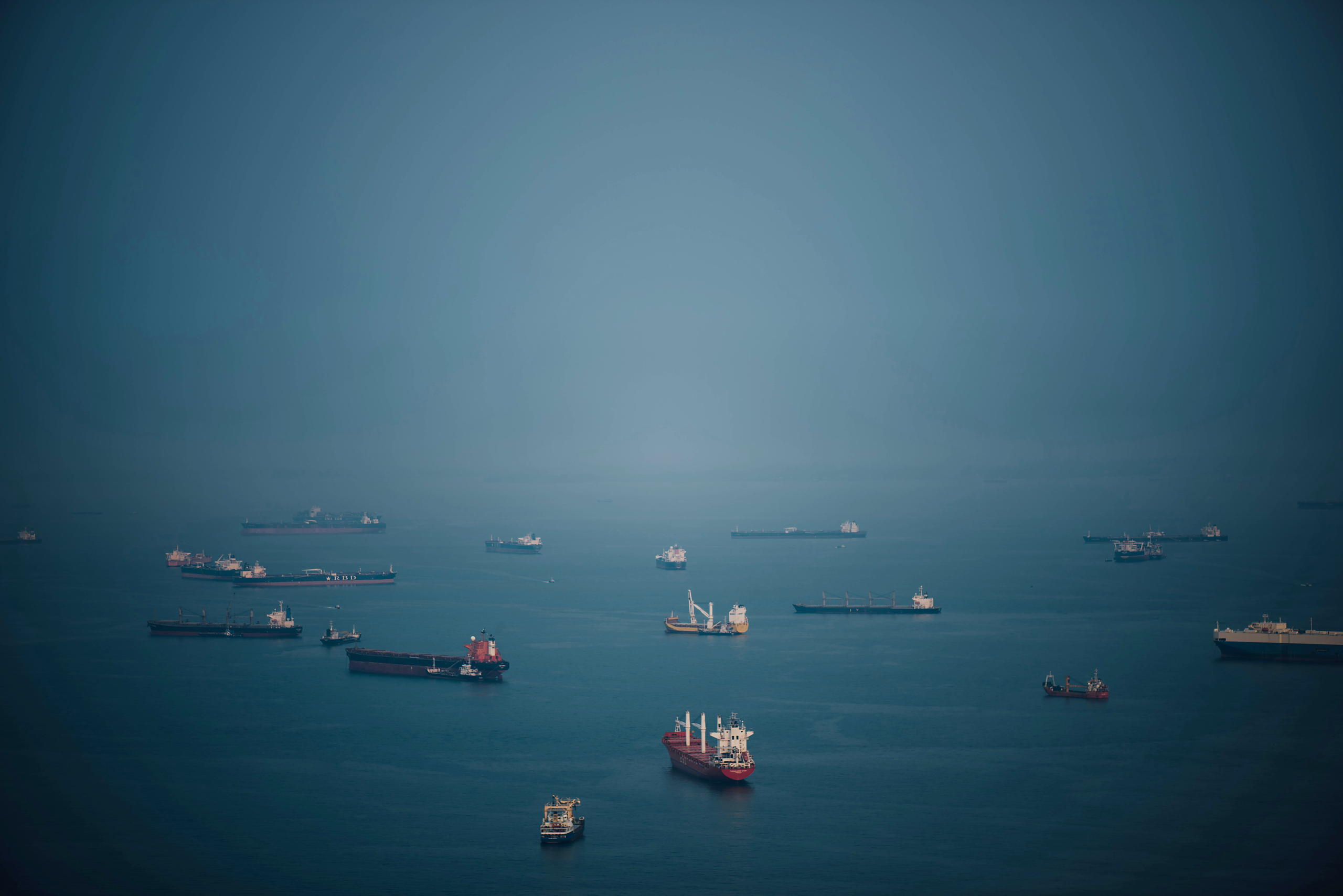 Bulk carriers riding at anchor across a blue-grey roadstead.