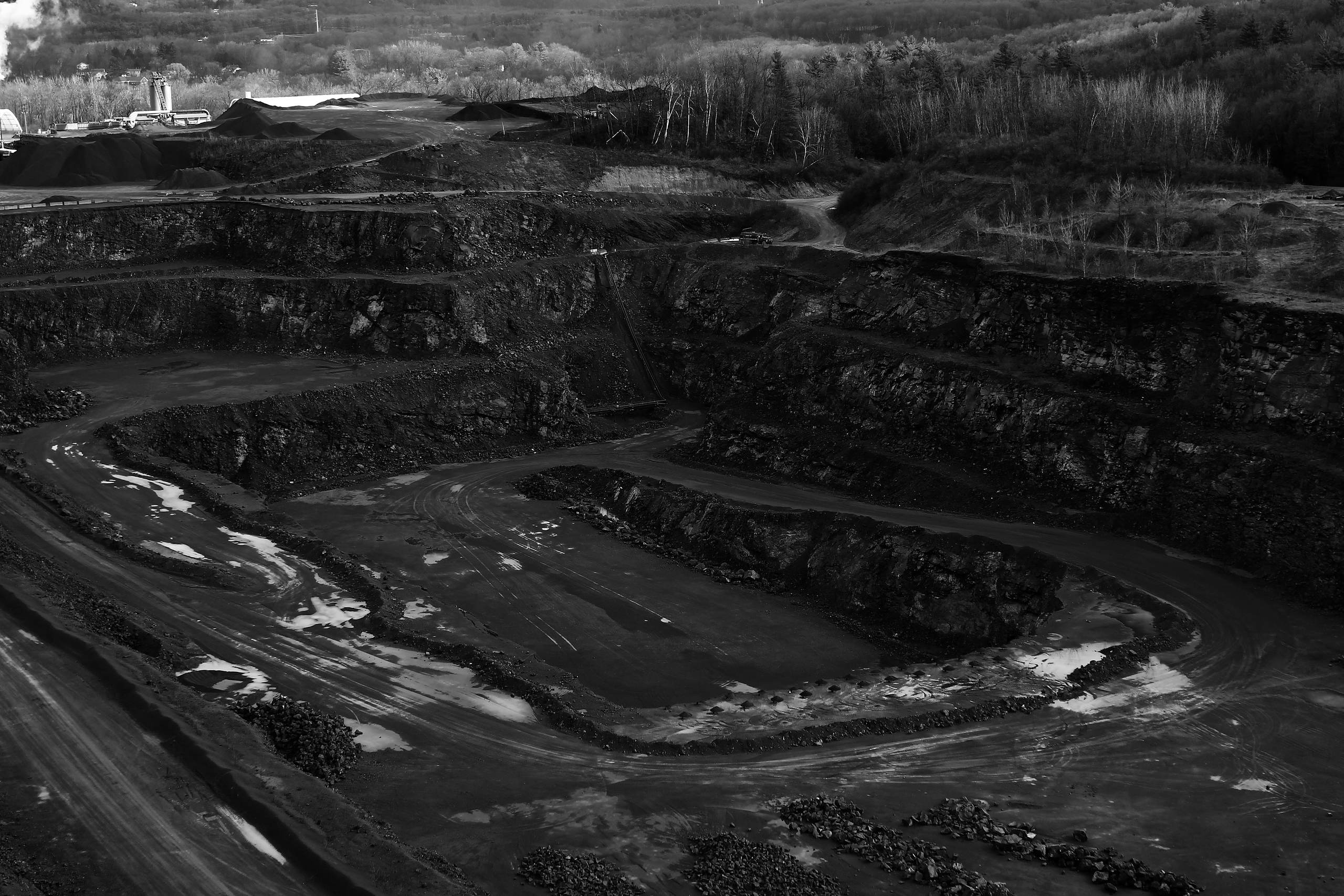 An open-pit mine seen from above, with dark stockpiles and haul roads.